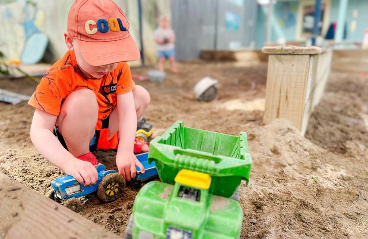 Evolve Education Preschool boy playing with trucks in the sandpit at daycare