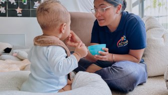 Evolve Education Teacher feeding baby boy in the nursery space at daycare