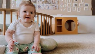 Evolve Education Baby girl sitting with pillow in nursery space at daycare