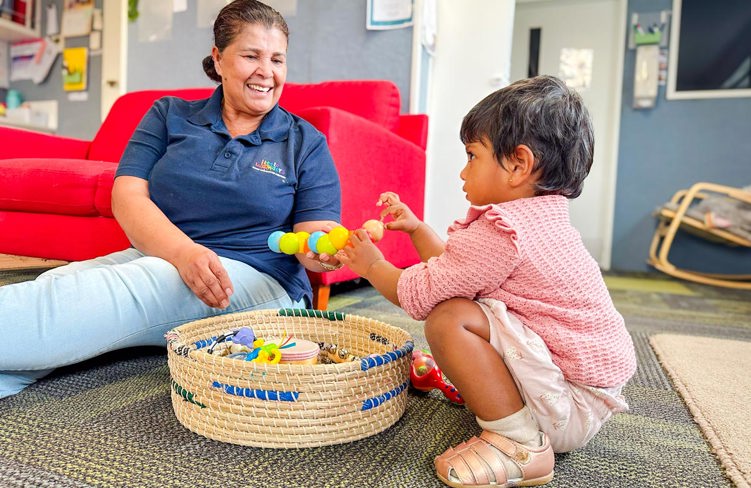 Evolve Education Teacher smiling with toddler playing with toys in basket