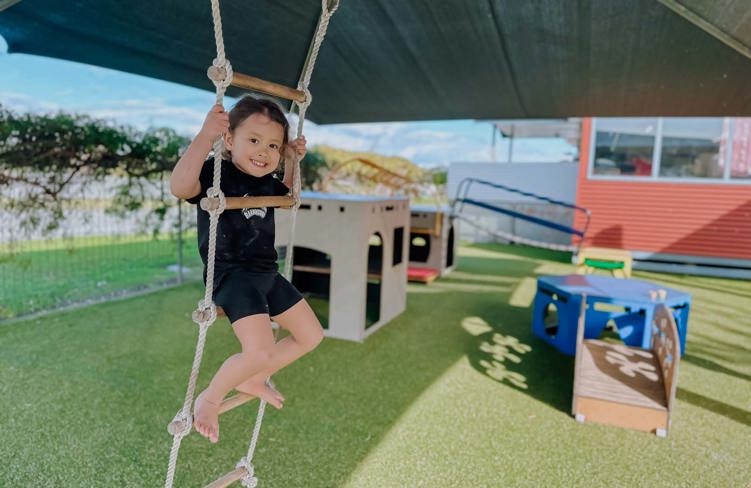 Evolve Education Preschool girl playing on ladder in playground at daycare